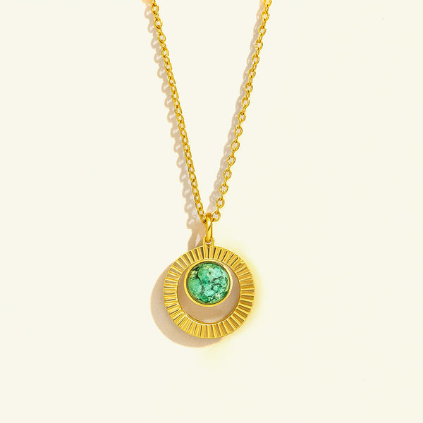 Gold necklace with a green gemstone pendant on a light beige background